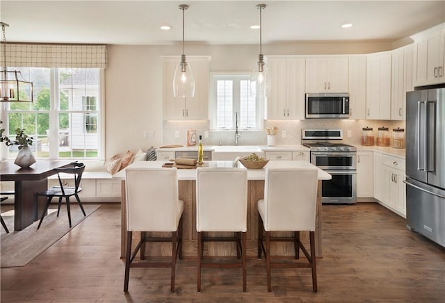 kitchen with white cabinets, a kitchen island, stainless steel appliances, and decorative light fixtures