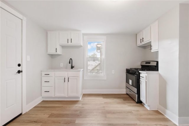 kitchen featuring white cabinets, light hardwood / wood-style flooring, stainless steel gas range oven, and sink