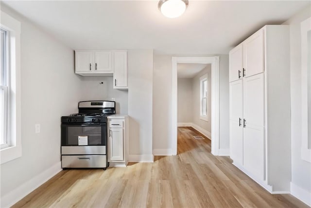 kitchen with a wealth of natural light, white cabinetry, light hardwood / wood-style floors, and stainless steel gas range