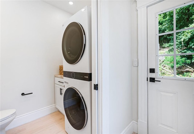 washroom featuring stacked washer and dryer, a healthy amount of sunlight, and light hardwood / wood-style floors