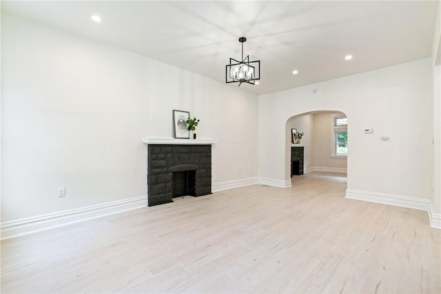 unfurnished living room featuring a stone fireplace, light hardwood / wood-style floors, and an inviting chandelier