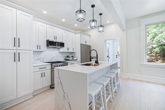 kitchen featuring backsplash, stainless steel appliances, a kitchen island with sink, decorative light fixtures, and white cabinetry