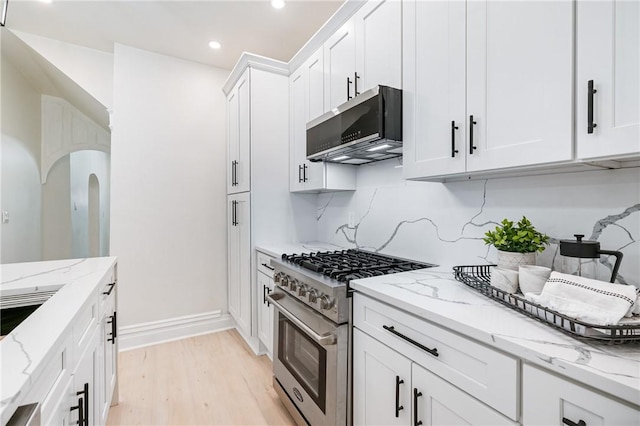 kitchen featuring white cabinets, light wood-type flooring, appliances with stainless steel finishes, tasteful backsplash, and light stone counters