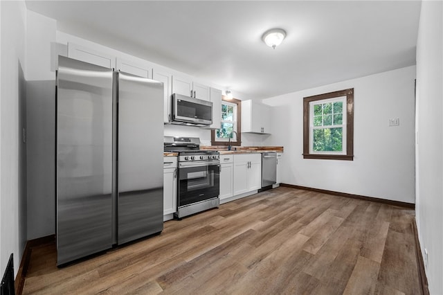 kitchen with white cabinets, sink, appliances with stainless steel finishes, and light hardwood / wood-style flooring