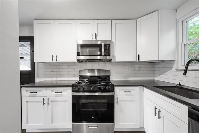 kitchen with appliances with stainless steel finishes, tasteful backsplash, sink, dark stone countertops, and white cabinets