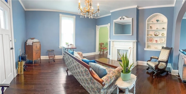 sitting room with built in shelves, dark wood-type flooring, a premium fireplace, a notable chandelier, and crown molding