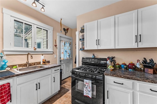 kitchen featuring white cabinets, black gas range oven, dark stone counters, and sink