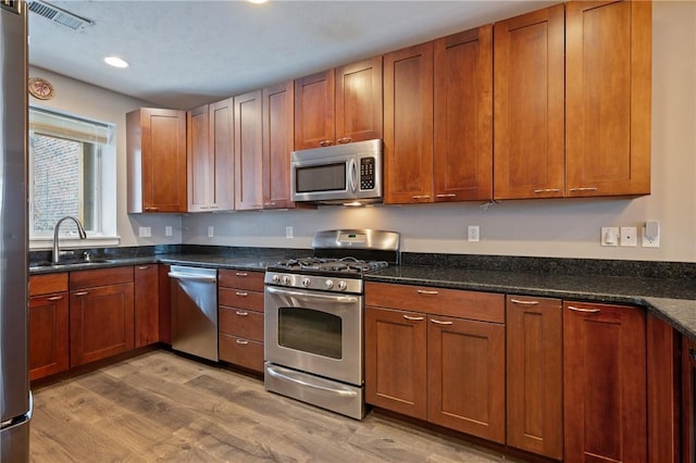 kitchen with appliances with stainless steel finishes, light hardwood / wood-style floors, dark stone counters, and sink