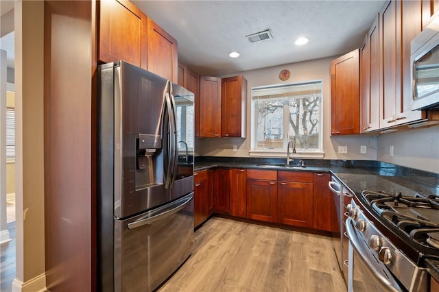 kitchen featuring appliances with stainless steel finishes, light hardwood / wood-style floors, dark stone countertops, and sink