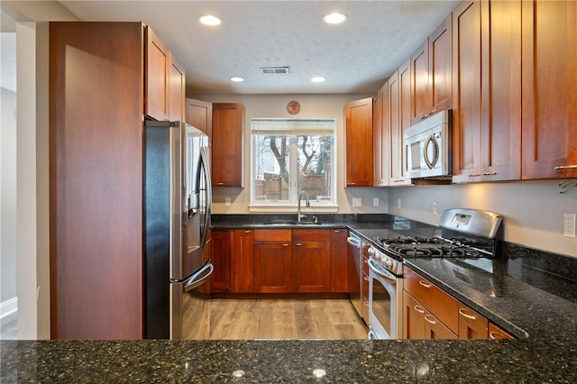 kitchen with dark stone countertops, sink, stainless steel appliances, and light hardwood / wood-style floors