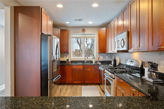 kitchen with dark stone countertops, sink, light hardwood / wood-style floors, and appliances with stainless steel finishes