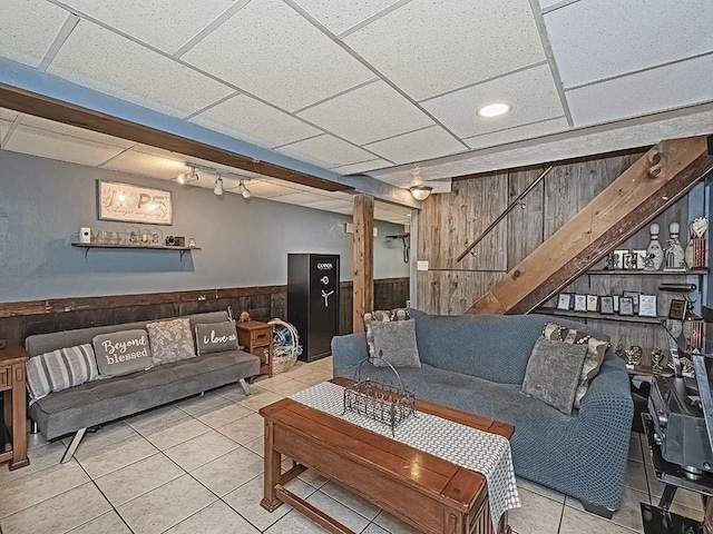 living room with tile patterned flooring, a drop ceiling, and wood walls