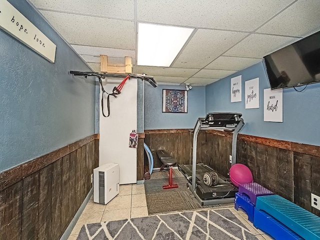 workout room with tile patterned floors, wooden walls, and a drop ceiling