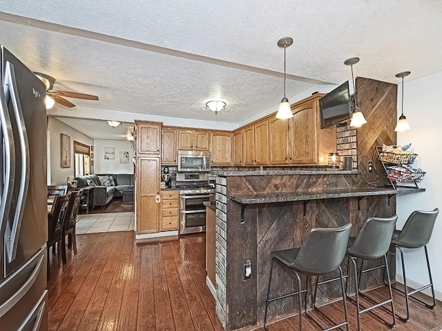 kitchen with pendant lighting, ceiling fan, appliances with stainless steel finishes, a kitchen bar, and kitchen peninsula