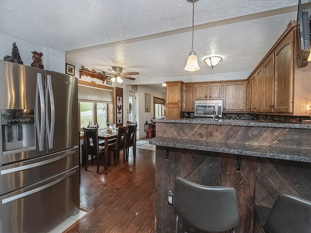 kitchen with ceiling fan, stainless steel appliances, a kitchen breakfast bar, pendant lighting, and a textured ceiling