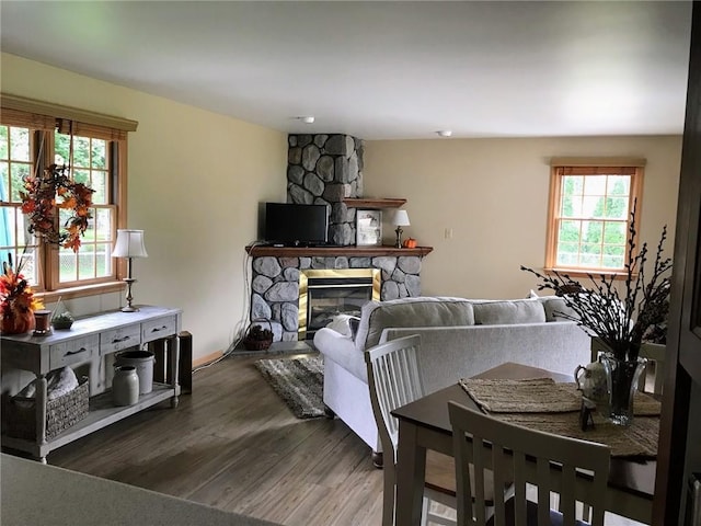 living room featuring a stone fireplace, a wealth of natural light, and dark wood-type flooring