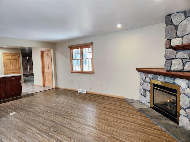 unfurnished living room featuring light hardwood / wood-style flooring and a stone fireplace