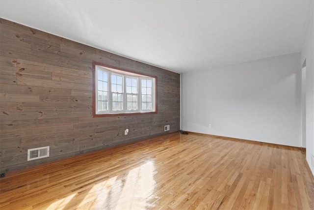 empty room with light hardwood / wood-style floors and wooden walls