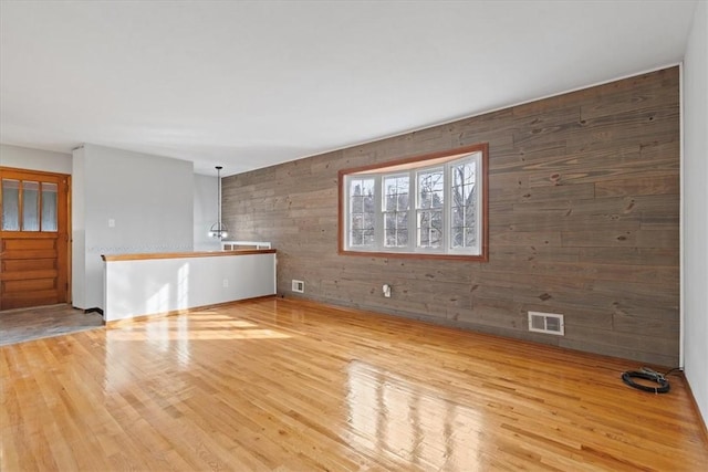 unfurnished room with light wood-type flooring and wooden walls