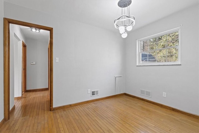 empty room featuring a chandelier and light hardwood / wood-style flooring