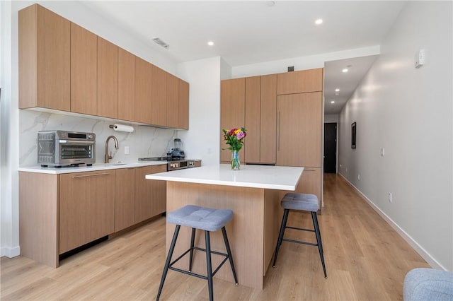 kitchen with decorative backsplash, light wood-type flooring, a kitchen island, and a breakfast bar area