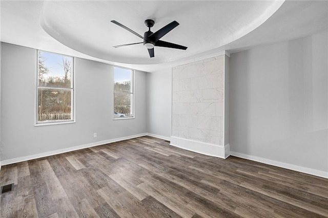 unfurnished room featuring a tray ceiling, ceiling fan, and dark hardwood / wood-style flooring