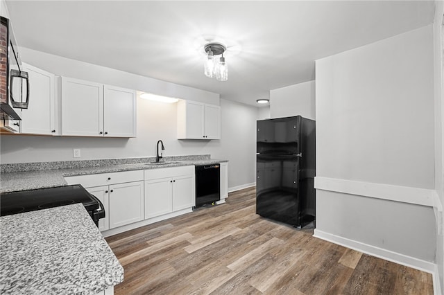 kitchen featuring white cabinetry, sink, light stone counters, black appliances, and light wood-type flooring