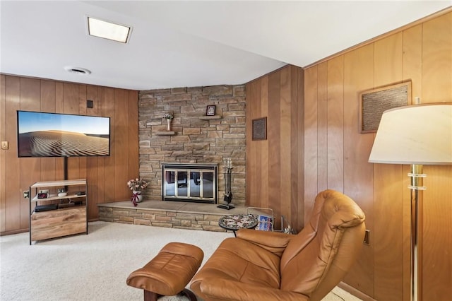 carpeted living room with a stone fireplace and wood walls