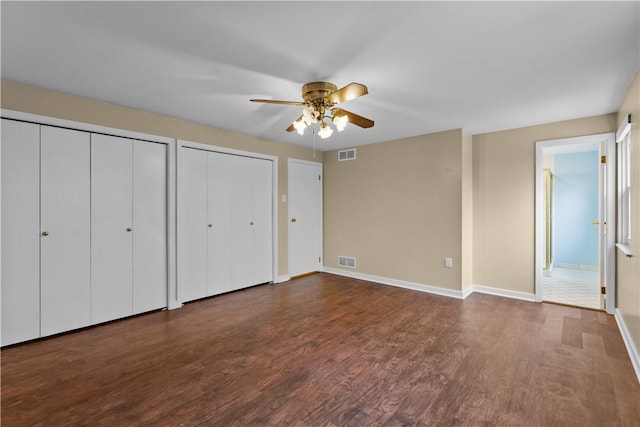 unfurnished bedroom featuring multiple closets, ceiling fan, dark hardwood / wood-style flooring, and ensuite bath