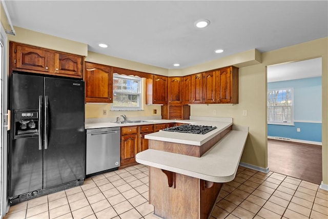 kitchen with kitchen peninsula, stainless steel appliances, sink, light tile patterned floors, and a breakfast bar area