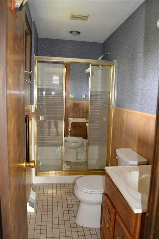 bathroom with tile patterned floors, toilet, wooden walls, vanity, and a shower with shower door