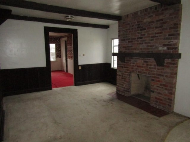 unfurnished living room with carpet flooring, beam ceiling, a fireplace, and wooden walls