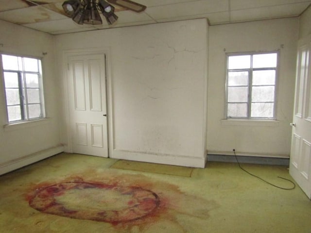 empty room featuring ceiling fan, a drop ceiling, a healthy amount of sunlight, and a baseboard heating unit