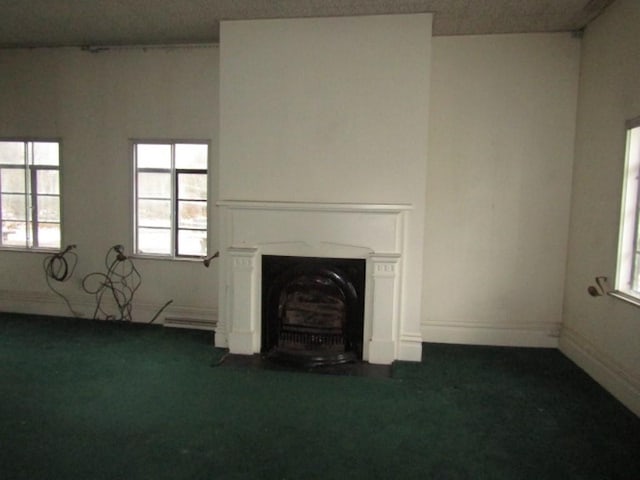 unfurnished living room with dark colored carpet, a wealth of natural light, and a baseboard heating unit