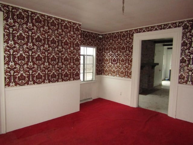 carpeted spare room featuring a fireplace and a baseboard heating unit