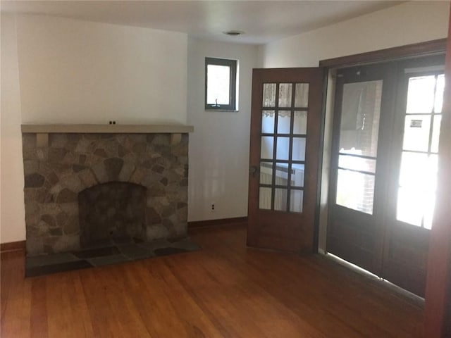 unfurnished living room with dark hardwood / wood-style flooring, french doors, a healthy amount of sunlight, and a stone fireplace