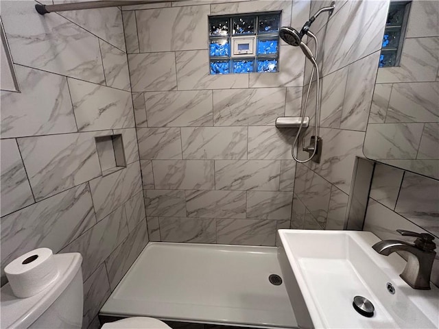 bathroom with sink, a tile shower, and toilet