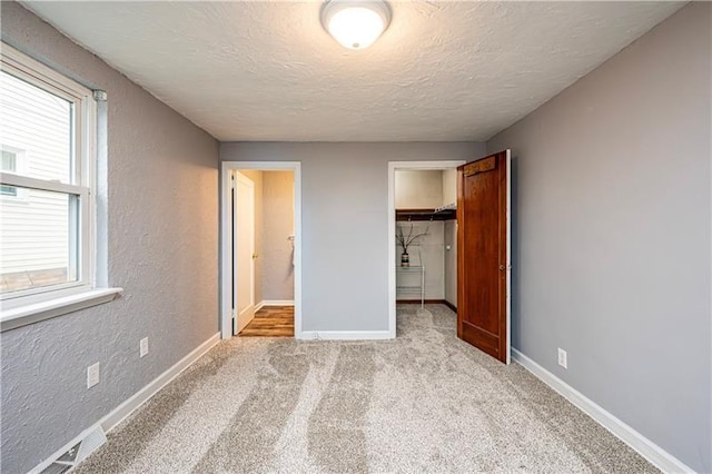 unfurnished bedroom featuring light carpet, a textured ceiling, a closet, and a walk in closet