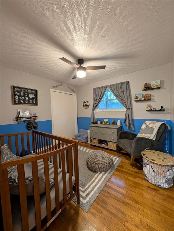 bedroom with ceiling fan, a nursery area, a textured ceiling, and wood-type flooring