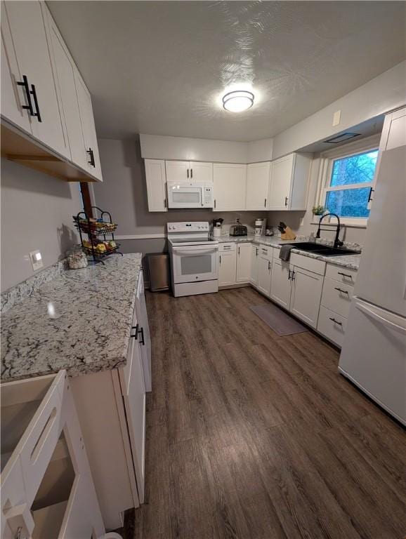 kitchen with light stone countertops, white appliances, sink, white cabinets, and dark hardwood / wood-style floors