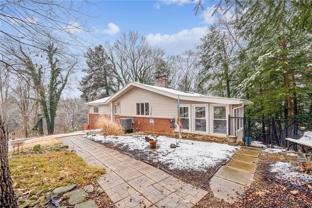 snow covered rear of property with central AC and a sunroom