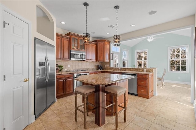 kitchen featuring ceiling fan, a center island, stainless steel appliances, lofted ceiling, and a kitchen bar