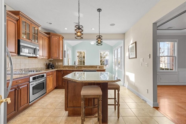 kitchen with pendant lighting, light tile patterned flooring, decorative backsplash, appliances with stainless steel finishes, and a kitchen island