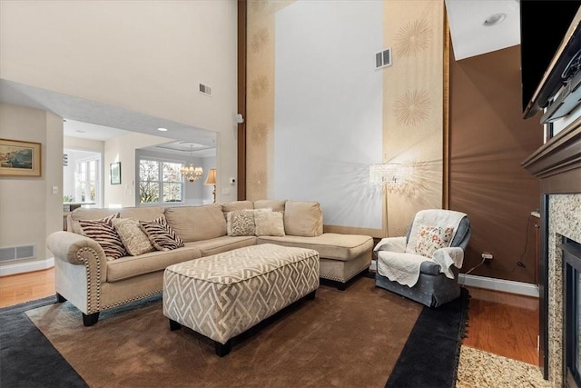 living room featuring a notable chandelier, dark hardwood / wood-style flooring, a high ceiling, and a tiled fireplace