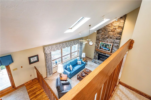 living room featuring ceiling fan, wood-type flooring, lofted ceiling with skylight, and a fireplace