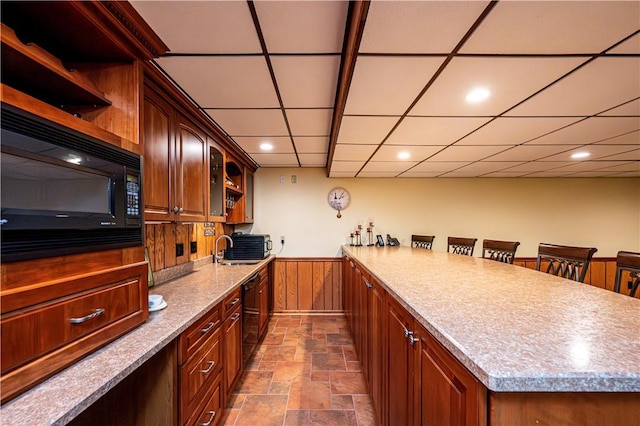 kitchen featuring sink, wood walls, a breakfast bar, a kitchen island, and black appliances