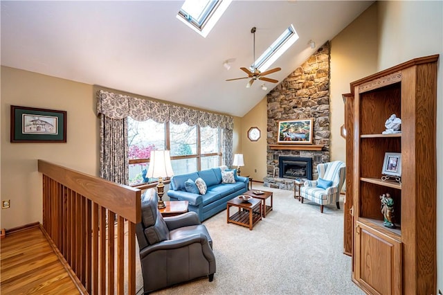 living room with a skylight, ceiling fan, high vaulted ceiling, light hardwood / wood-style floors, and a stone fireplace