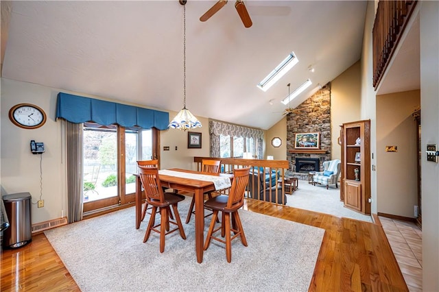 dining space with a skylight, ceiling fan, light hardwood / wood-style flooring, high vaulted ceiling, and a fireplace