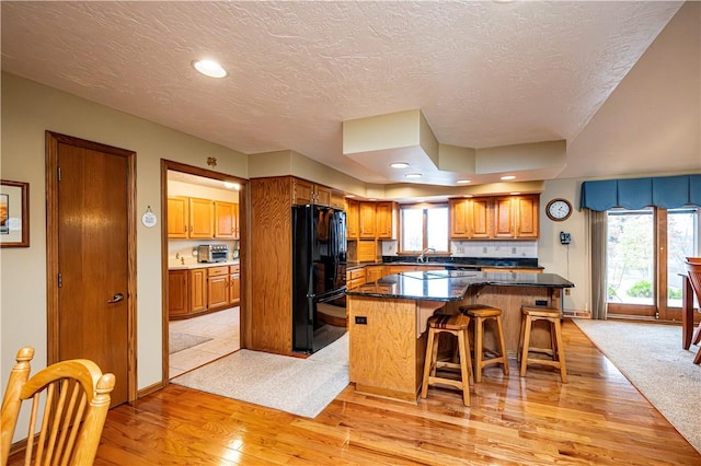 kitchen with a kitchen breakfast bar, black fridge, a textured ceiling, a kitchen island, and light wood-type flooring