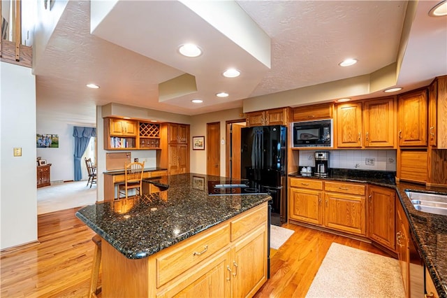 kitchen with dark stone counters, a center island, black appliances, and light hardwood / wood-style floors